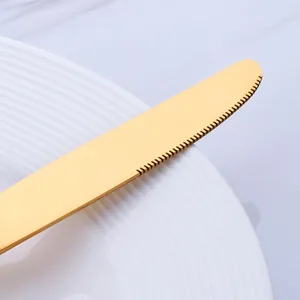 Couteau de table doré en acier inoxydable 304 avec lame dentelée sur assiette