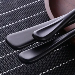 Détail du manche ergonomique noir mat en acier inoxydable 304 sur une assiette bois