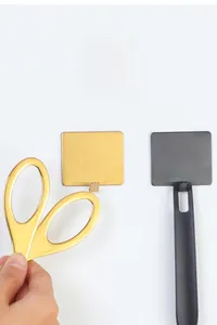 Detail of square adhesive stainless steel hooks in gold and black holding kitchen tools