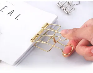 Close-up of hand holding a hollow gold metal binder clip over a minimalist white book