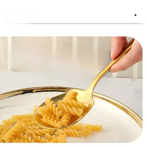 Detail of a golden stainless steel serving spoon held over a plate of pasta in a kitchen