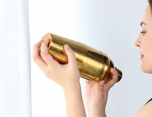 Golden stainless steel cocktail shaker held by hands with water droplets and mirror finish