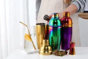 Action shot of pouring cocktail from gold stainless steel shaker with strainer and tools