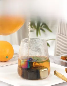 Close-up of colored stainless steel ice cubes with golden tongs in a glass of tea
