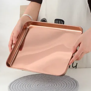 Gros plan d'un plateau rectangulaire en acier inoxydable or rose tenu à la main
