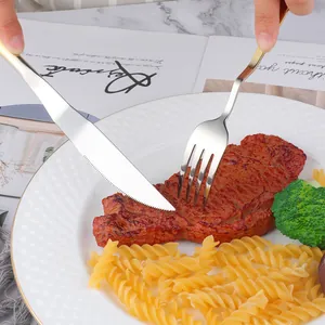 Close-up of gradient gold stainless steel knife and fork cutting a steak on a dinner plate