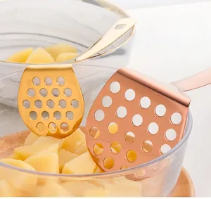 Detail of stainless steel potato masher with fine round holes and gold titanium finish