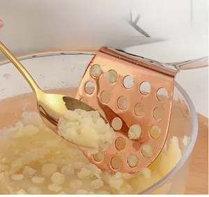 Rose gold stainless steel potato masher with hole design used in a glass bowl