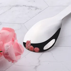 Gros plan d'une cuillère en acier poli miroir sur marbre blanc avec accents floraux