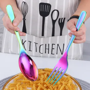 Detail of hand holding rainbow plated stainless steel serving spoon and fork with pasta
