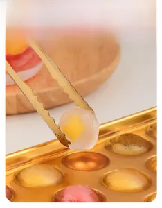 Spherical stainless steel ice mold with gold tongs and fruit-filled round ice balls