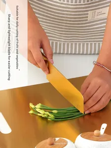 Close-up of golden stainless steel chef knife slicing fresh green scallions on cutting board