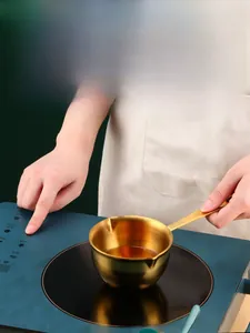 Close-up of golden stainless steel mini pot with dual spouts for melting on induction hob