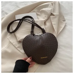 Close-up of heart-shaped dark brown crossbody bag with crocodile texture and gold zippers
