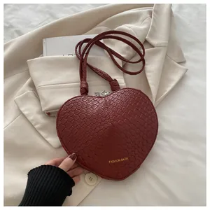 Detail of heart-shaped burgundy crossbody bag with crocodile texture and gold lettering
