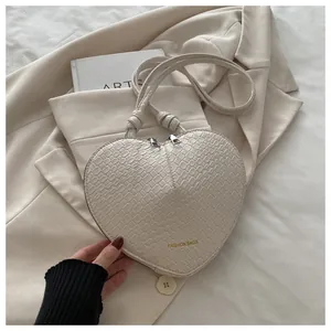 Macro shot of cream heart bag featuring crocodile texture and gold fashion bags lettering