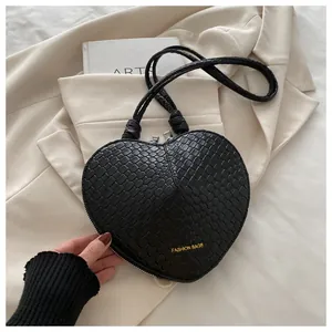 Detailed view of black heart-shaped bag with woven texture and gold fashion logo