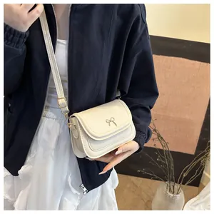Close-up of the beige crossbody bag featuring a golden bow metal buckle and flap cover