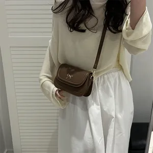 Caramel faux leather crossbody bag with a gold bow clasp on a white background