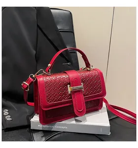 Detail shot of the red woven flap and metallic square clasp on a small square crossbody bag
