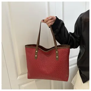 Detail of red woven texture tote bag featuring brown handles and gold rivet accents