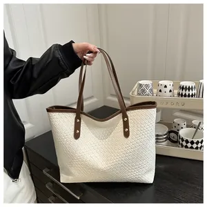 Detail of white woven texture and brown leather strap with gold studs on a tote bag