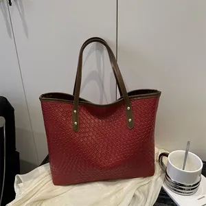 Deep red woven tote bag with brown straps and gold rivets in a minimalist indoor setting