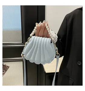 Détail du sac coquille bleu clair avec une poignée en perles et des accents dorés