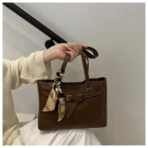 Détail d'un sac cabas en cuir marron foncé avec foulard en soie et boucle dorée élégante
