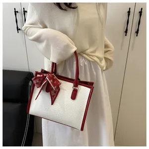 Close-up of white crocodile embossed tote bag with red handle and silk scarf detail