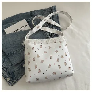 Détail d'un sac en toile blanc avec motif d'ours et bordure en dentelle sur du denim