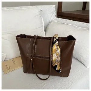 Detail of dark brown tote bag featuring white contrast stitching and a silk scarf handle