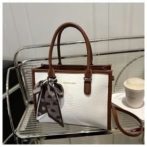 Detail of snake skin texture tote bag with brown handles and a decorative heart scarf