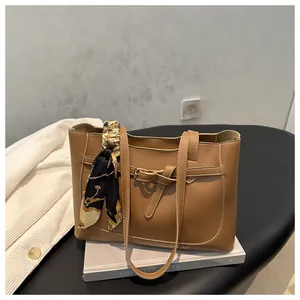 Détail d'un sac cabas en cuir marron orné d'un foulard soyeux et d'une boucle dorée