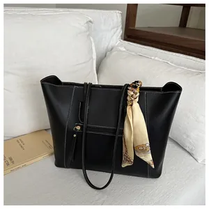 Detail of black leather tote bag with white contrast stitching and a silk scarf handle