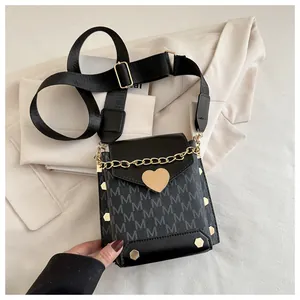 Detail of crossbody bag with golden heart clasp, M-letter print, and wide canvas strap