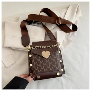 Close-up of heart-shaped metal buckle and M-pattern print on brown crossbody bag
