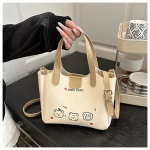 Détail d'un sac en cuir beige avec motifs d'ours et logo nœud rouge sur le devant