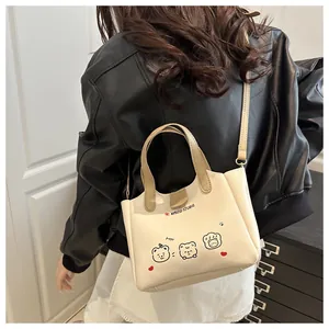Détail d'un sac cabas blanc crème avec imprimé ours porté sur une veste en cuir noir