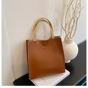 Close-up of a minimalist brown leather handbag featuring contrast cream handles and fine stitching