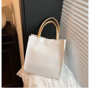 Close-up of a minimalist white leather tote bag with brown handles on lace fabric