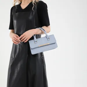 Sac à main rectangulaire bleu clair avec détails dorés porté par un mannequin
