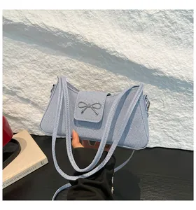 Détail du sac baguette en jean bleu clair avec boucle nœud argentée et doubles brides