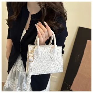 Detail of white crocodile embossed mini handbag with gold buckles and adjustable strap