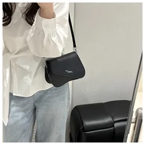 Close-up of black square crossbody bag featuring asymmetric flap with white lettering print