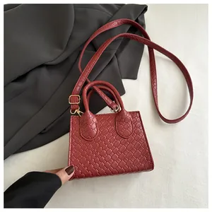 Detail of burgundy woven texture small handbag with golden metal buckles and straps