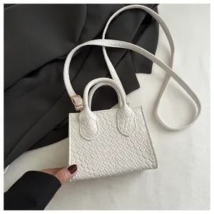 Detailed close-up of white crocodile embossed leather texture and golden buckle on mini bag