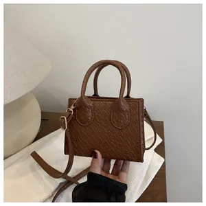 Detail of dark brown croc-effect mini square bag with gold hardware and top handles