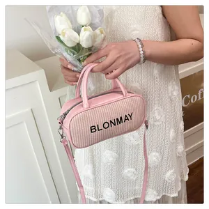 Close-up of light pink baguette bag with woven texture and logo held by a model