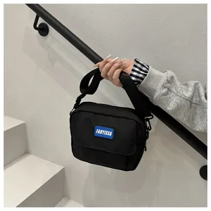 Détail d'un sac bandoulière en nylon noir avec étiquette bleue et sangle réglable